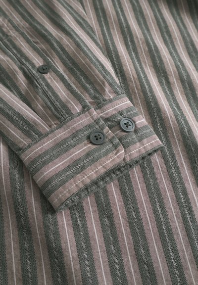 Raidallinen paita vihreissä ja vaaleanpunaisissa sävyissä, jossa on nappikiinnitteinen kalvosin tummilla napeilla ja kontrastitikkaus reunoissa.