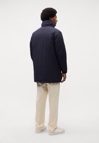 Giubbotto imbottito blu navy con colletto alto, maniche lunghe e taglio dritto. Tessuto liscio senza motivi visibili o dettagli hardware.