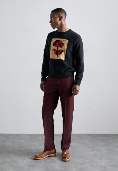 Čierny pletený sveter so zlatým a červeným kvetinovým vzorom, doplnený vínovými nohavicami a hnedými koženými topánkami. Jednoduchá textúra, priliehavý strih.