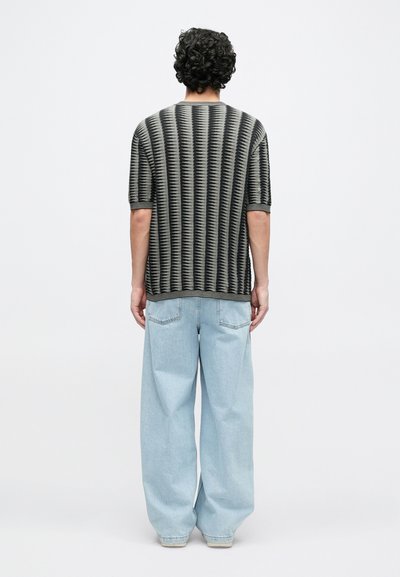 Chemise à manches courtes noire et grise avec un motif ondulé, associée à un jean large bleu clair, vue de dos.