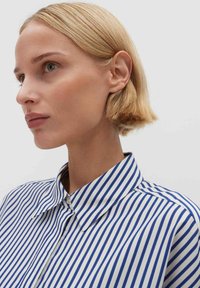 Hemd mit Knopfleiste, das vertikale blau-weiße Streifen zeigt, mit klassischem Kragen und glatter Stoffstruktur. Keine sichtbaren Muster oder Verzierungen.