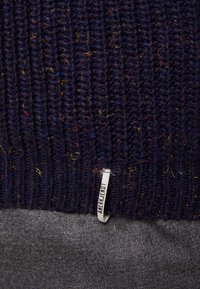 Mörk marinblått stickat tyg med flerfärgade fläckar och en liten vit tygbit med texten "AMERICAN EAGLE."