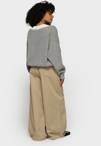 Pull en tricot côtelé gris avec des épaules abaissées, associé à un pantalon large beige décontracté, vu de dos. Design décontracté.