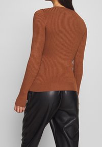 Suéter marrón de canalé con mangas largas y una silueta ligeramente ajustada, combinado con pantalones de cuero negros de tiro alto.