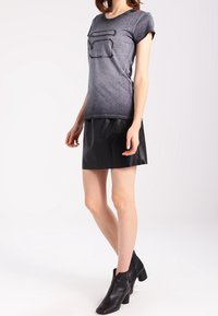 Grå t-shirt med korta ärmar som har en texturerad design på framsidan, i kombination med en svart läderskjorta och ankelskor.