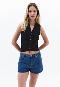 Svart ribbad ärmlös topp med knappar och krage, i kombination med högmidjade blå denimshorts med framfickor och en guldfärgad knapp.