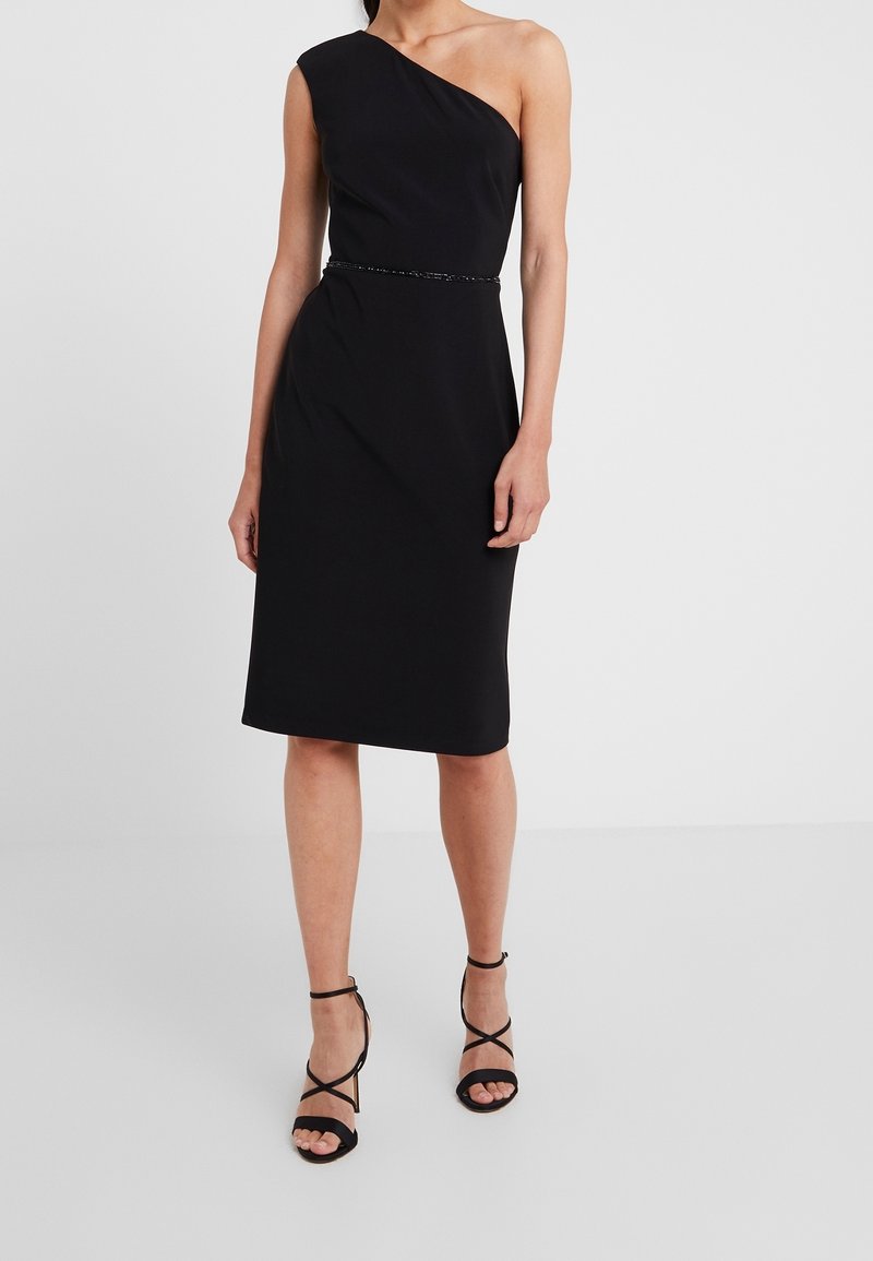 Svart axelbandslös klänning med figurnära silhuett, knälång längd och ett tunt, dekorativt bälte som framhäver midjan. Bärs med svarta sandaletter med remmar.