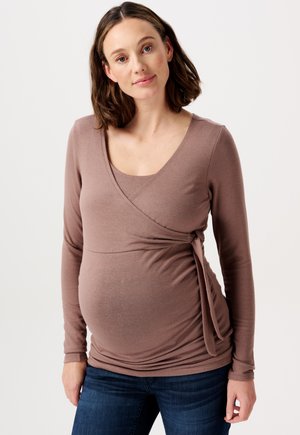 Braune langärmlige Wickelbluse mit V-Ausschnitt und seitlichem Bindedetail. Aus weichem Stoff gefertigt, fällt sie sanft über einen runden Bauch. Kombiniert mit Jeans.