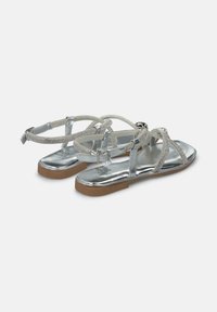 Zilveren platte sandalen met een glanzende afwerking, voorzien van gevlochten banden versierd met rhinestones en een bruine rubberen zool.