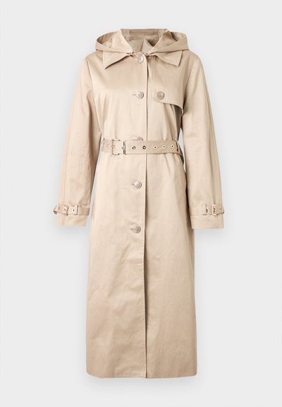 Trench-coat long beige avec capuche, fermeture à boutons, taille ceinturée et sangles ajustables aux poignets, présenté sur un fond uni.