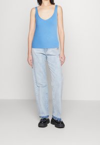 Modrý žebrovaný top bez rukávů s hlubokým výstřihem do V, doplněný o světlé rovné džíny a objemné černé platformové boty.