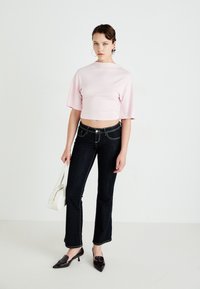 Lys rosa crop topp med korte ermer, parret med mørkeblå flagrende jeans med kontraststing og en liten hvit håndveske.