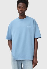 Vaaleansininen puuvillainen t-paita, jossa on pyöreä pääntie, lyhyet hihat ja rento malli. Vasemmassa rintamuksessa pieni logo.