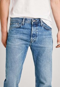 Světle modré džíny z denimu s rovným střihem, pěti kapsami, zipovým zapínáním a švy zdobícími pas a kapsy.