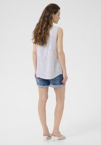Haut sans manches rayé blanc et marine associé à un short en jean déchiré. Accentué de poignets roulés et de talons blocs de couleur claire.