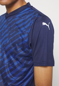 Blå mönstrad atletisk skjorta med en mörk marinblå bas, korta ärmar och en vit Puma-logga på axeln.