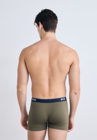 Boxeri scurți de culoare verde măsliniu cu un brâu elastic bleu închis, pe care apare logo-ul "BOSS". Textură netedă și design ajustat, văzute din spate.
