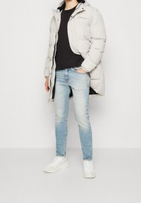 Ljusgrå fodrad jacka med huva och dragkedja, svart t-shirt, ljusblå jeans och vita sneakers. Platta texturer och avslappnad stil.