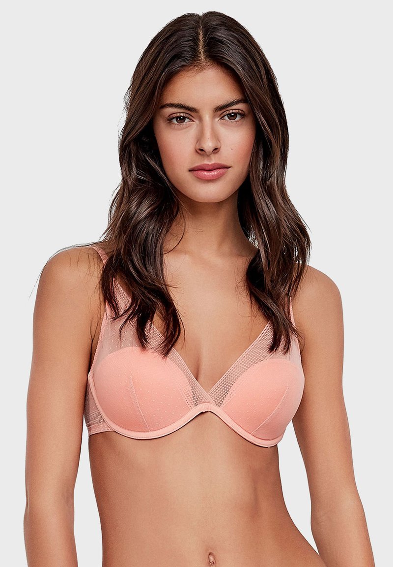 Soutien-gorge en tissu pêche doux à pois, avec un soutien-gorge à armatures, des accents en mesh sur les bonnets et un décolleté en V. Texture lisse dans l'ensemble.