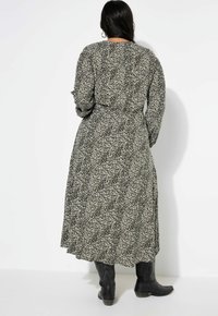 Maxikleid im Schwarz-Weißen Blumenmuster, mit langen Ärmeln, einem taillierten Bund und einem fließenden Rock, der über schwarzen Knöchelstiefeln endet.