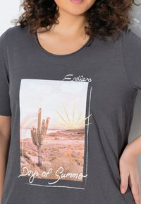 Grijze T-shirt met een grafische print van een woestijnscene met een cactus, zon en bergen, gelabeld "Eindeloze Dagen van de Zomer" in witte tekst.