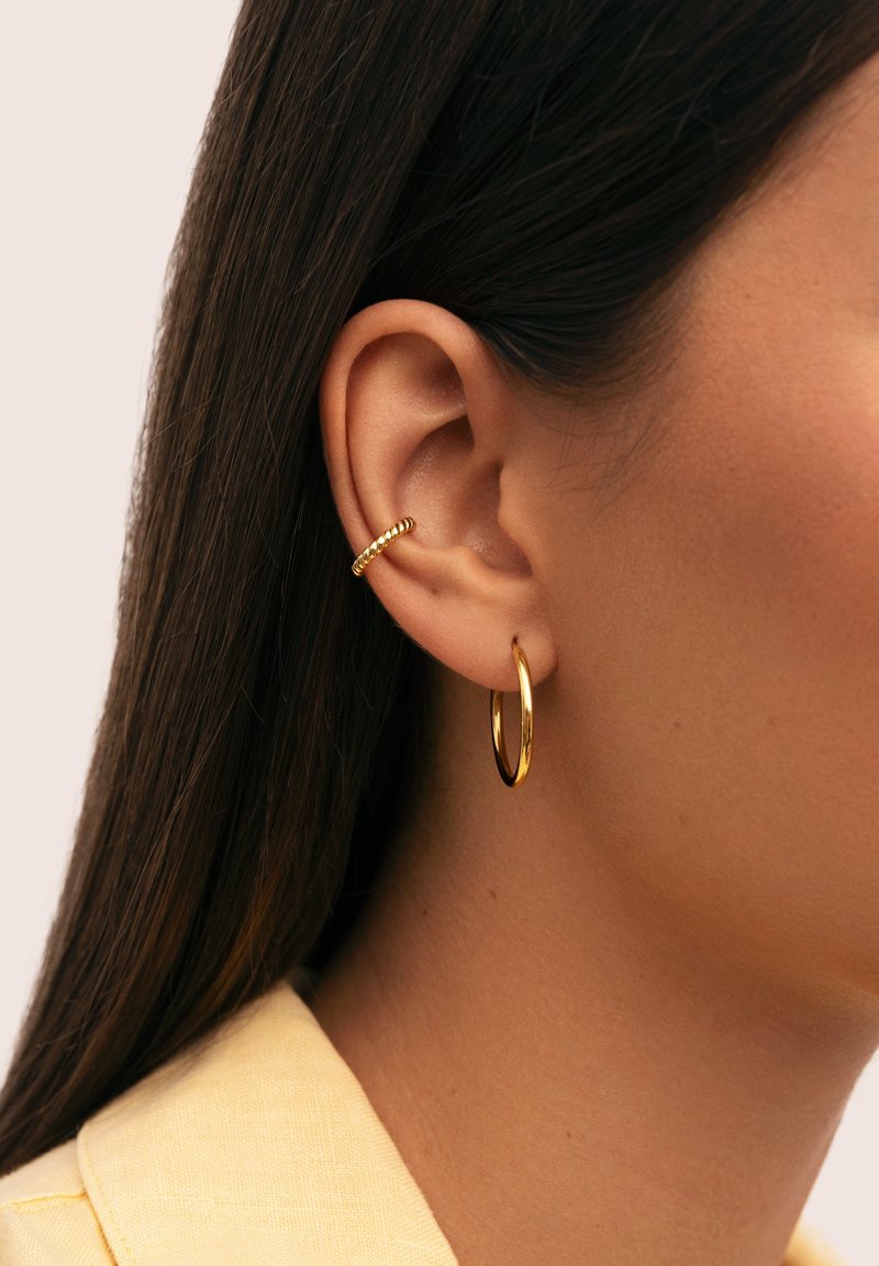 Pendientes de aro dorados con un acabado suave y un aro para la oreja en forma de cuerda trenzada. Vista en primer plano que enfatiza los detalles de diseño y color.