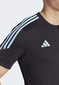 Camiseta deportiva negra con diseño de tres franjas azul claro en los hombros. Presenta un cuello redondo y un pequeño logo blanco en el pecho. Tela suave y ajustada.
