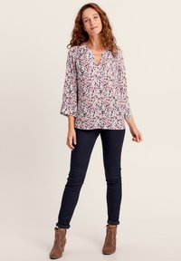 Blusa floreale con maniche a campana lunghe in tonalità di rosa, blu e verde; scollatura a V; tessuto leggero; abbinata a jeans skinny scuri e stivaletti marroni.