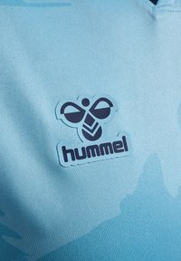 Blå sportsstof med et mørkeblåt stiliseret bi-logo og "hummel" brandnavn trykt på det.