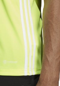 Heldere gele sportshirt met witte strepenaccenten. Deze heeft een gladde textuur, een aansluitend ontwerp en beschikt over "AEROREADY" merknaam dichtbij de zoom.