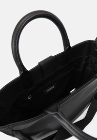 Svart handväska med dubbla handtag, tillverkad av mjukt material. Insidan har en dragkedja, logotags och en elegant, avskalad design.
