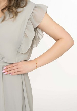 Light grey ruffled dress with a smooth texture; gold bracelet featuring red and clear beads. Model's hand placed on her waist.