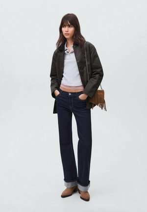 Chaqueta verde oscuro, polo gris claro, jeans azul oscuro, puños remangados, botas de tobillo marrones y un bolso marrón con flecos y cadena.
