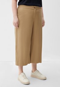 Beige wijde pantalon met een soepele textuur, zijzakken en een sluiting met een knoop aan de voorkant, gecombineerd met witte sneakers.