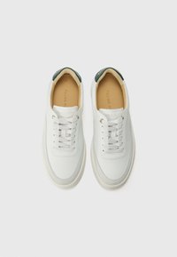 Baskets en cuir blanc à texture lisse, bout rond et lacets plats. Présentent un accent vert au talon et une doublure intérieure beige.