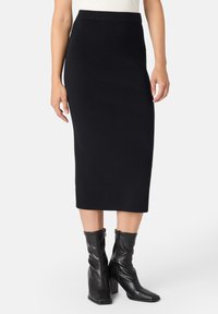 Jupe midi noire à côtes avec une coupe ajustée et une taille élastique, associée à des bottes noires à talons montantes.