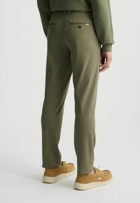 Pantalones de color verde oliva con una textura suave, ajuste ceñido y dos bolsillos traseros, complementados con zapatos de ante beige con suela blanca.