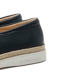 Chaussures noires en cuir sans lacets avec une semelle intermédiaire en jute de style espadrille et une semelle en caoutchouc blanc, présentant une texture lisse et des bords arrondis.