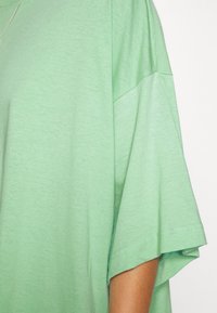 Camiseta verde menta hecha de algodón suave con costuras en los hombros caídas y un corte relajado. Textura suave, detalle de costura mínima en los bordes.