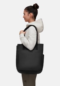Sac fourre-tout noir avec des poignées robustes, fabriqué dans un matériau durable, présentant une texture lisse et une poche latérale pour un espace de rangement supplémentaire.