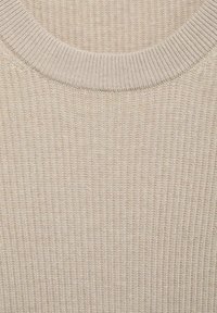 Tissu en tricot côtelé beige avec un col rond, présentant un motif texturé et une finition lisse. Matière douce et extensible.