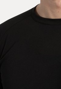 Czarna bawełniana koszula z długim rękawem, okrągłym dekoltem i subtelną teksturą, ukazująca zbliżenie tkaniny oraz szczegóły szwu na ramieniu.