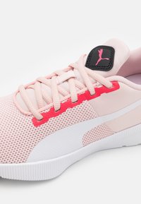 Scarpa da ginnastica rosa chiaro con tomaia in rete, accenti bianchi e dettagli rossi sui lati. Presenta lacci e una linguetta nera con il marchio vicino alla linguetta.