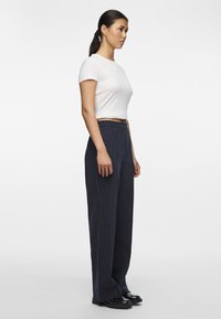 Weißes Kurzarmhemd kombiniert mit dunkelblau gestreiften, weit geschnittenen Hosen mit hoher Taille und glattem Material. Schwarze Schuhe mit dickem Sohlen.