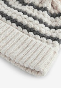 Bonnet en crème avec des rayures grises foncées. Présente un motif tressé texturé et un poignet côtelé. Apparence douce et semblable à de la laine.