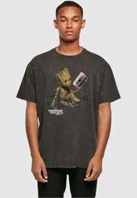 Camiseta negra de gran tamaño hecha de algodón, con un diseño impreso de Groot sosteniendo una cinta de casete, con el texto "Guardianes de la Galaxia Vol. 2".