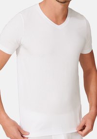 Weißes Kurzarm-V-Neck-Shirt aus glattem, leichtem Stoff. Der figurbetonte Schnitt betont den Oberkörper mit einem schlichten, minimalistischen Design.
