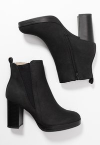 Botas negras de tobillo con un acabado suave de ante sintético, paneles laterales elásticos, un zipper vertical y un tacón grueso y texturizado.