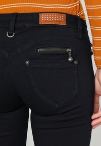Vaqueros oscuros de corte slim, con un bolsillo con cremallera y costuras en contraste. Parche de cuero de la marca en la cintura.