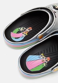 Sabots en caoutchouc gris avec un graphique coloré des Powerpuff Girls à l'intérieur, dotés d'une semelle extérieure noire texturée et d'une semelle intermédiaire rayée multicolore.